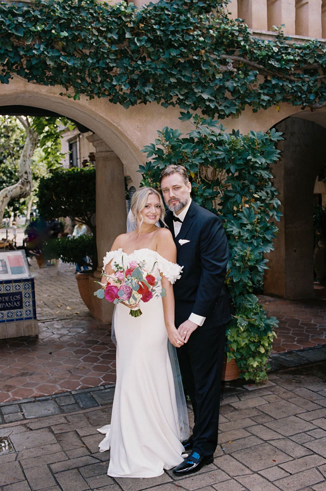 Bride and groom standing together beneath ivy-covered arches with Spanish-style architecture during a micro wedding at Tlaquepaque.