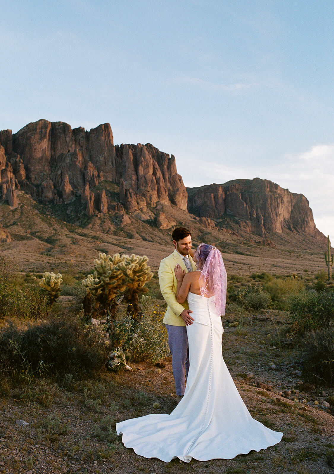 Bride and groom embracing in the Arizona desert during a colorful sunset elopement with dramatic mountain scenery