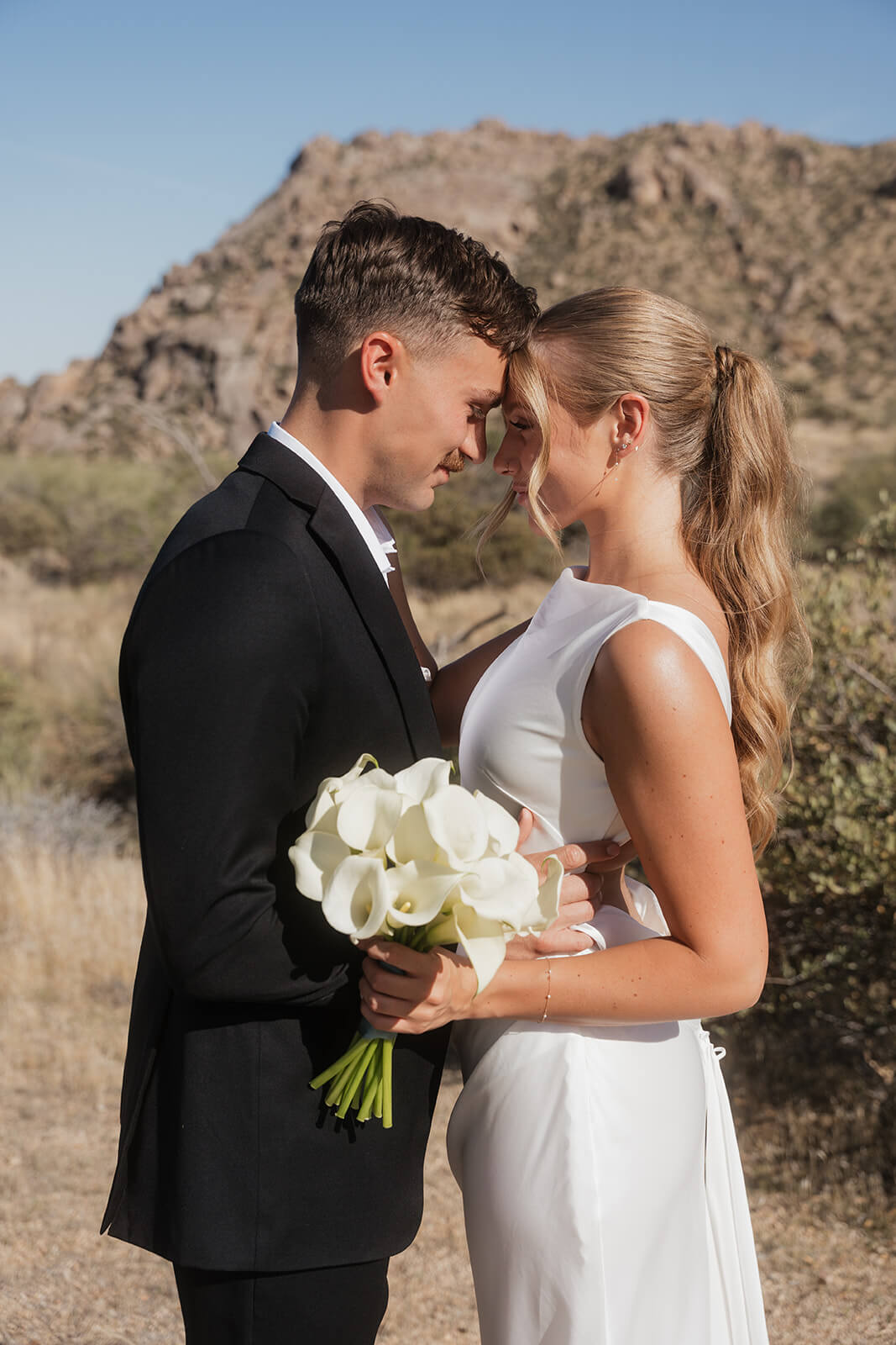 Couple holding each other in the desert during an intimate micro wedding with mountain views and modern bridal style