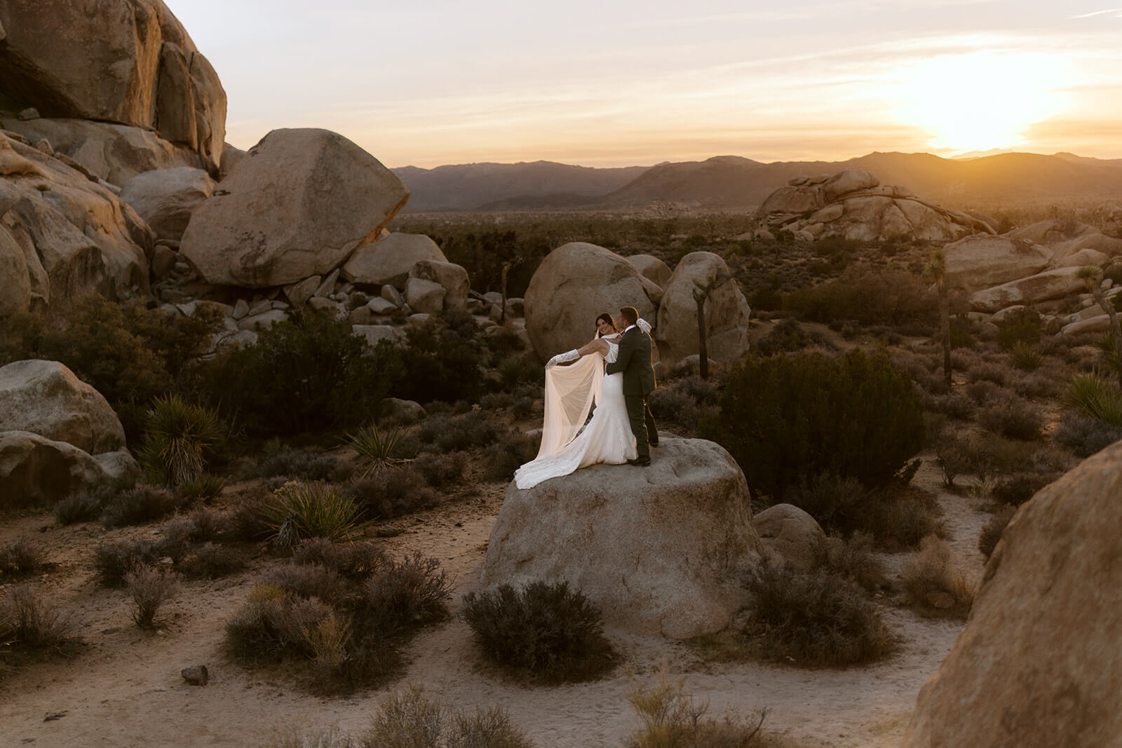 Bride and groom standing on boulders during a romantic Joshua Tree elopement at sunset