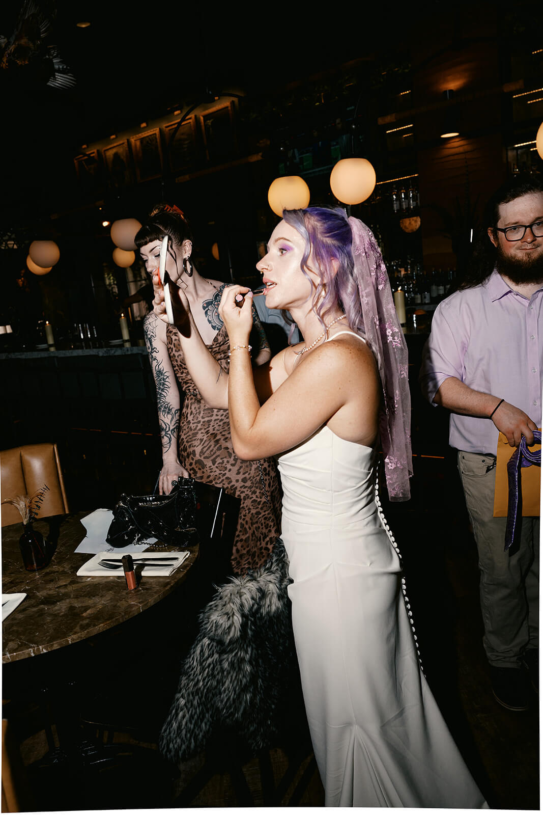 Bride getting ready with bold purple makeup before a playful modern elopement reception