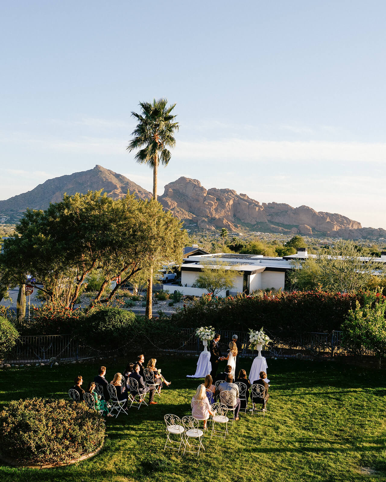 Wide view of a luxury backyard micro wedding ceremony with desert mountains, intimate guest seating, and romantic floral arrangements