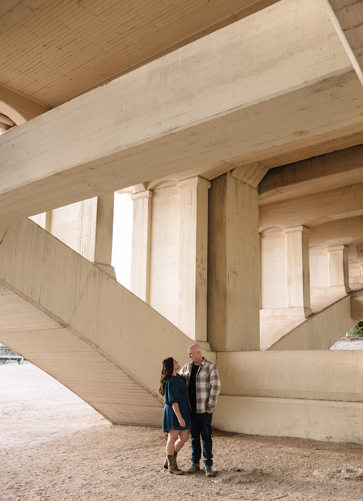 A couple stands close together under the concrete arches of the Tempe Town Lake bridge, one of the most unique engagement photoshoot locations in the Phoenix area.