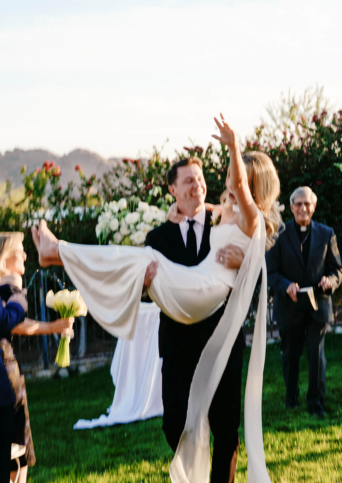 Groom lifting bride in celebration after their outdoor micro wedding ceremony with mountain views and sunset light