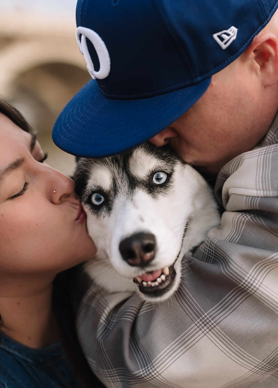 A close up of a couple pressing their faces into their husky dog from both sides, the dog looking wide eyed at the camera.