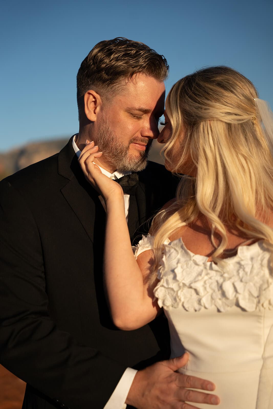 Bride and groom embracing during sunset with red rock mountains blurred in the background during a Sedona wedding session.
