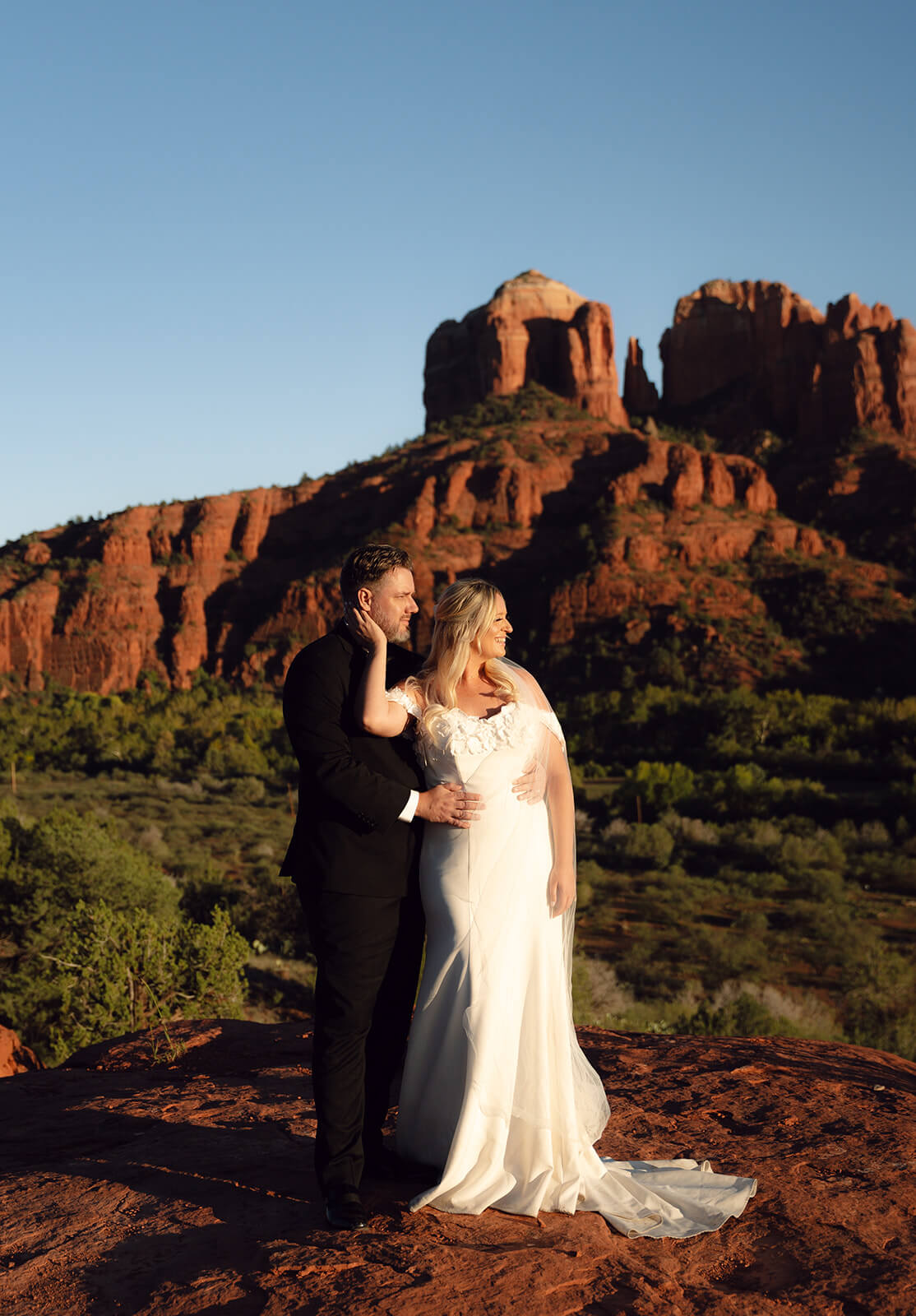 Couple embracing on red rock cliffs during a golden hour elopement in Sedona surrounded by dramatic desert scenery