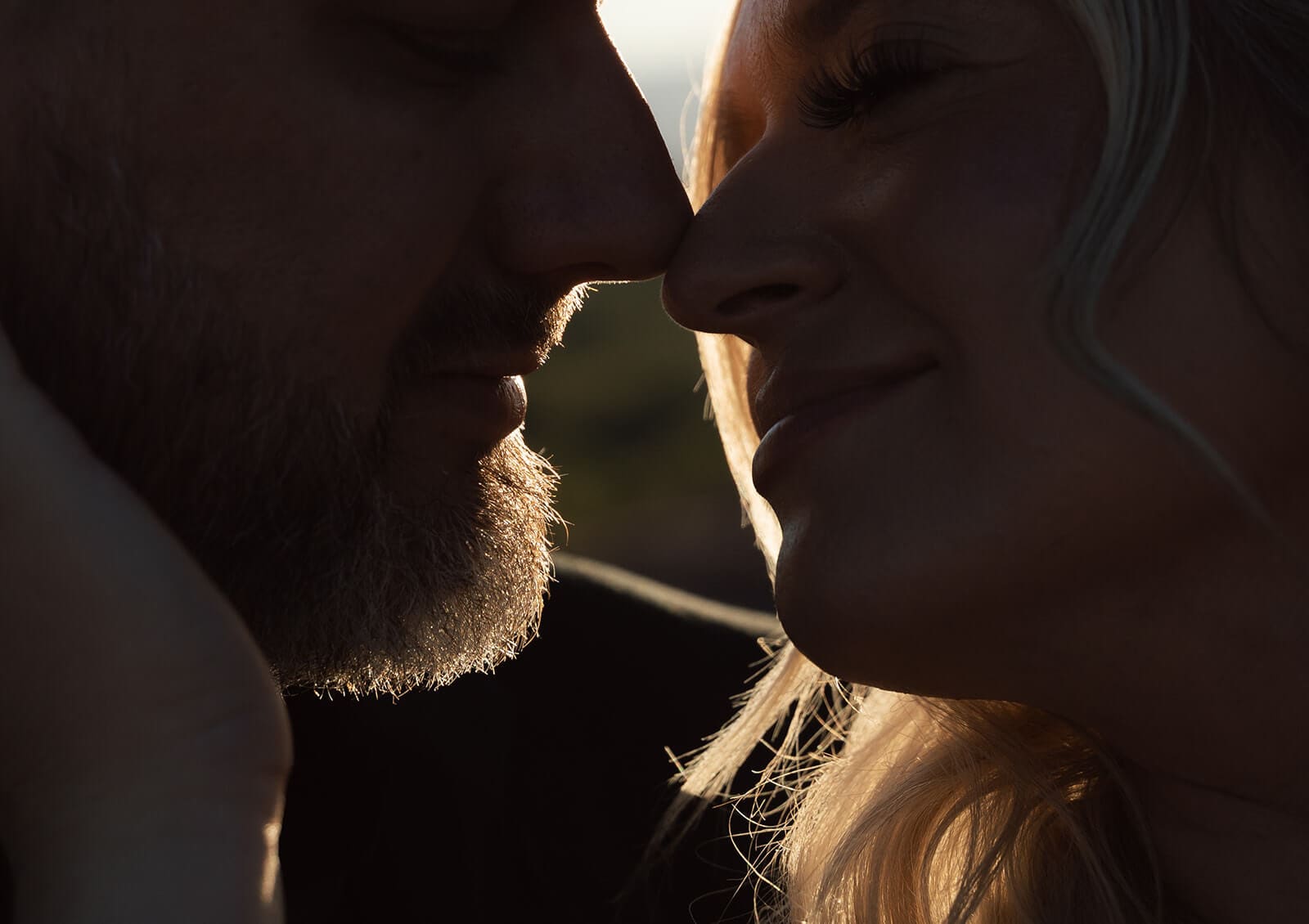 Close-up portrait of the bride and groom touching foreheads during golden hour with soft sunlight illuminating their faces.