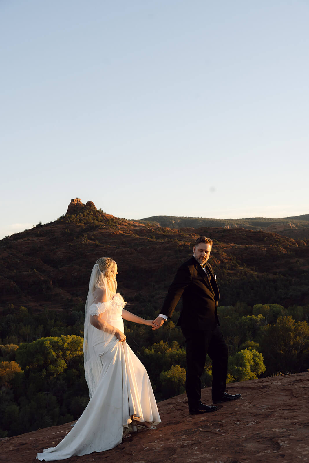 Couple walking hand in hand across red rock cliffs during a romantic desert elopement at sunset