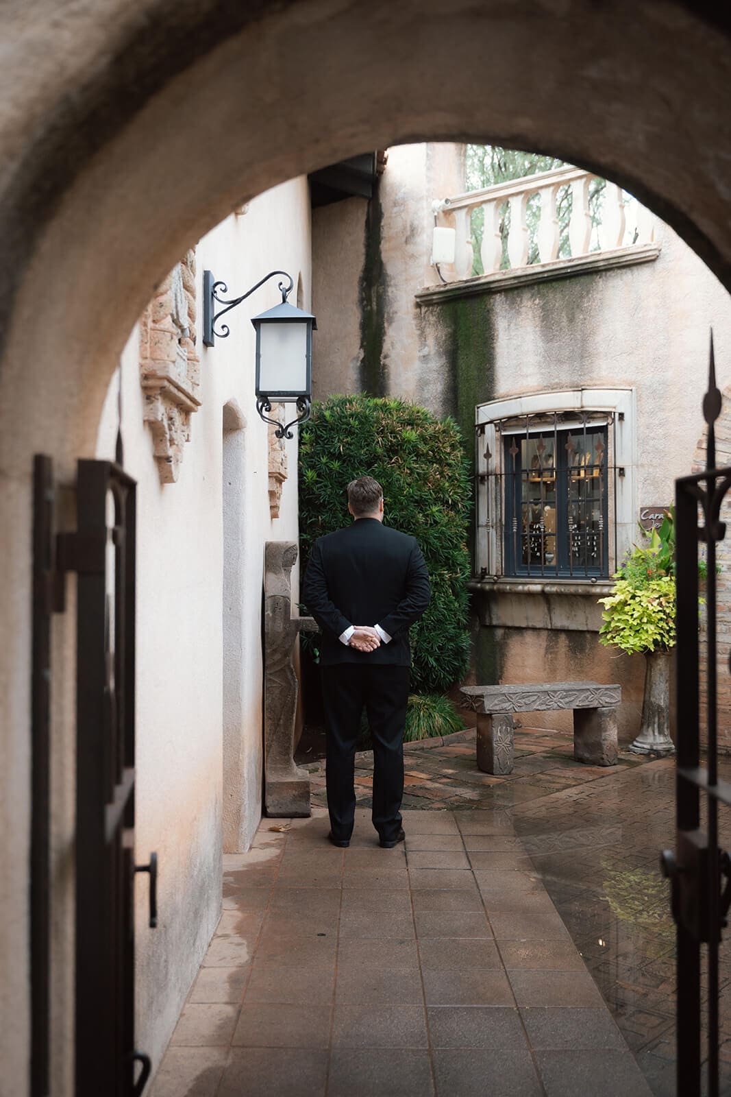 Groom standing beneath a stone archway with his hands behind his back before a first look during a micro wedding at Tlaquepaque.