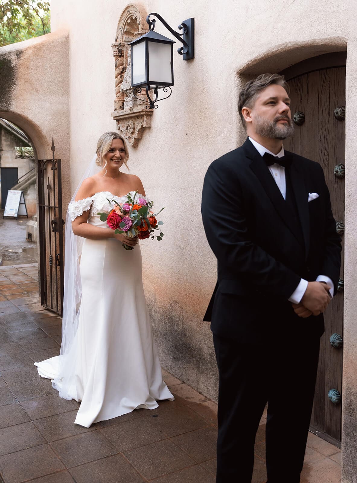 Bride approaching the groom from behind for a first look beside a stucco wall during a micro wedding at Tlaquepaque.