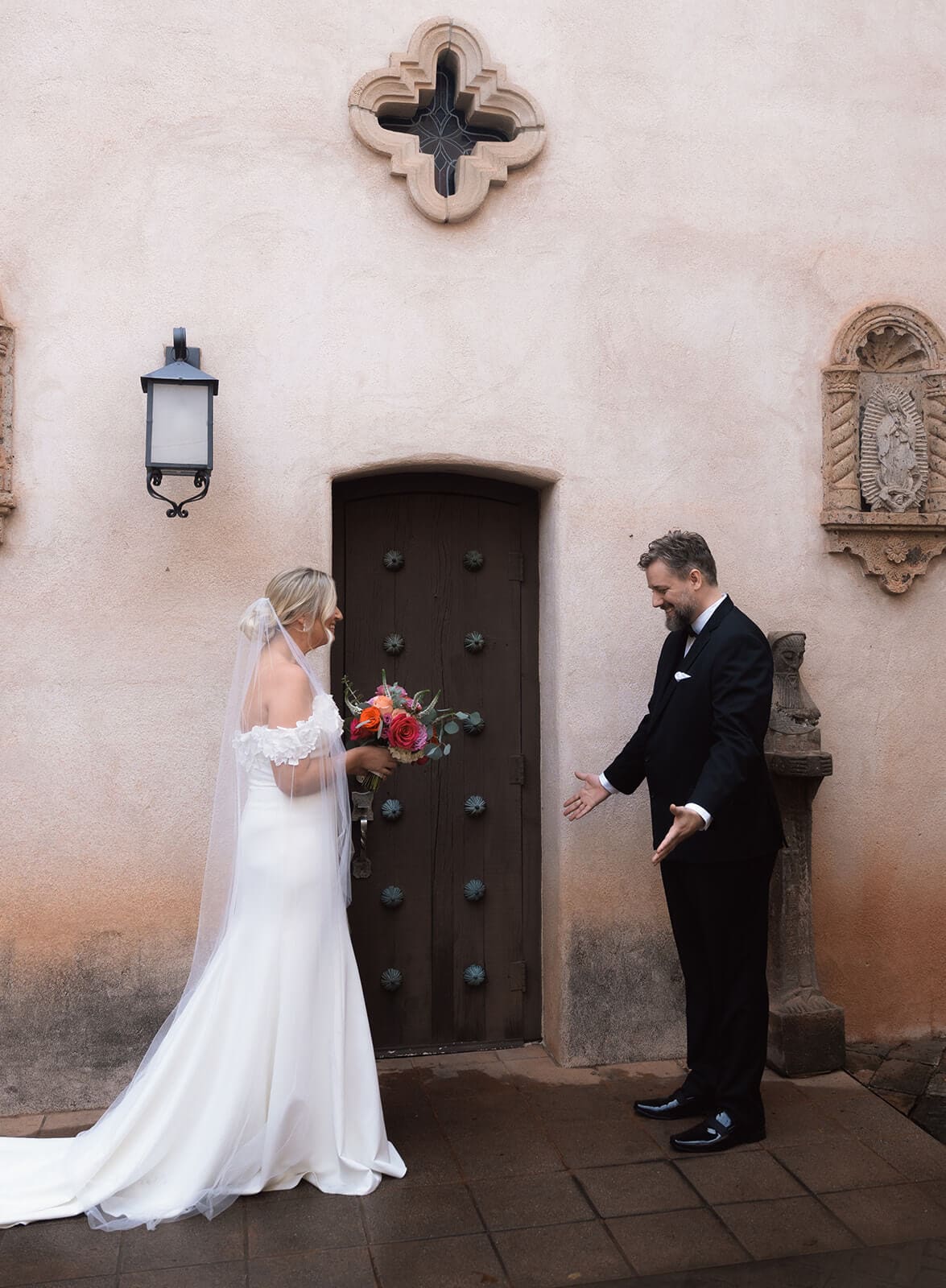 Bride and groom turning toward each other during their first look in front of a large wooden door at Tlaquepaque.