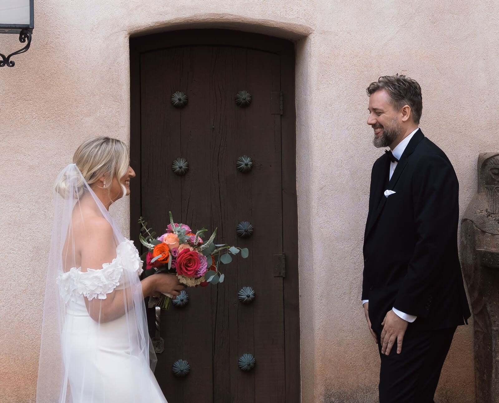 Bride and groom sharing a first look in front of a large wooden door during a micro wedding at Tlaquepaque, with the bride holding a colorful bouquet.