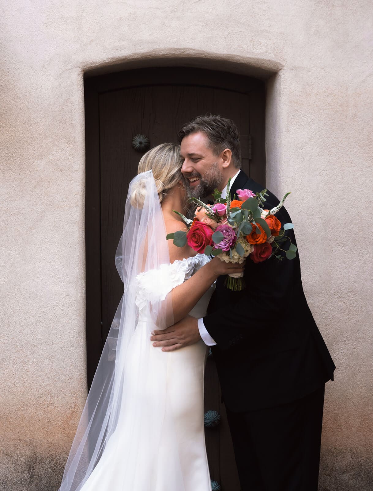 Bride and groom embracing in front of a carved wooden door during a micro wedding at Tlaquepaque.