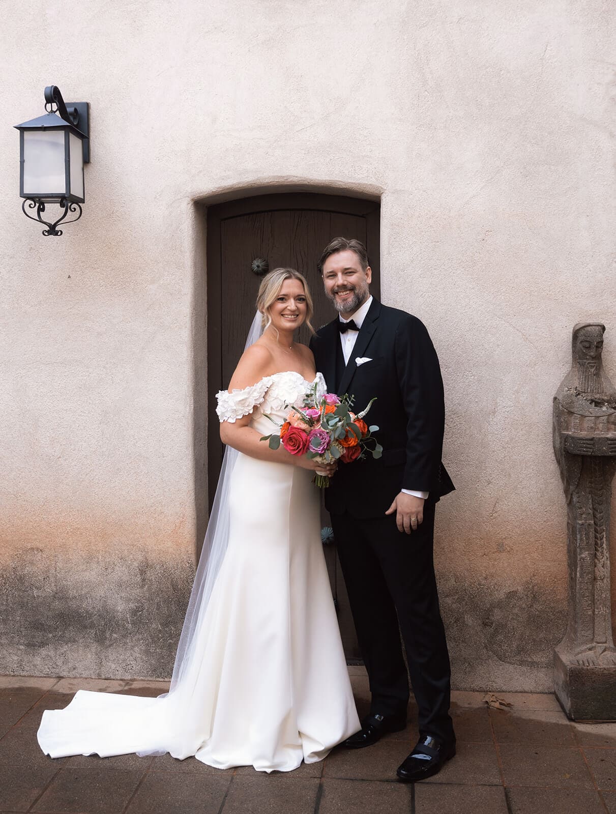 Bride and groom standing together and smiling in front of a stucco wall during a micro wedding at Tlaquepaque.