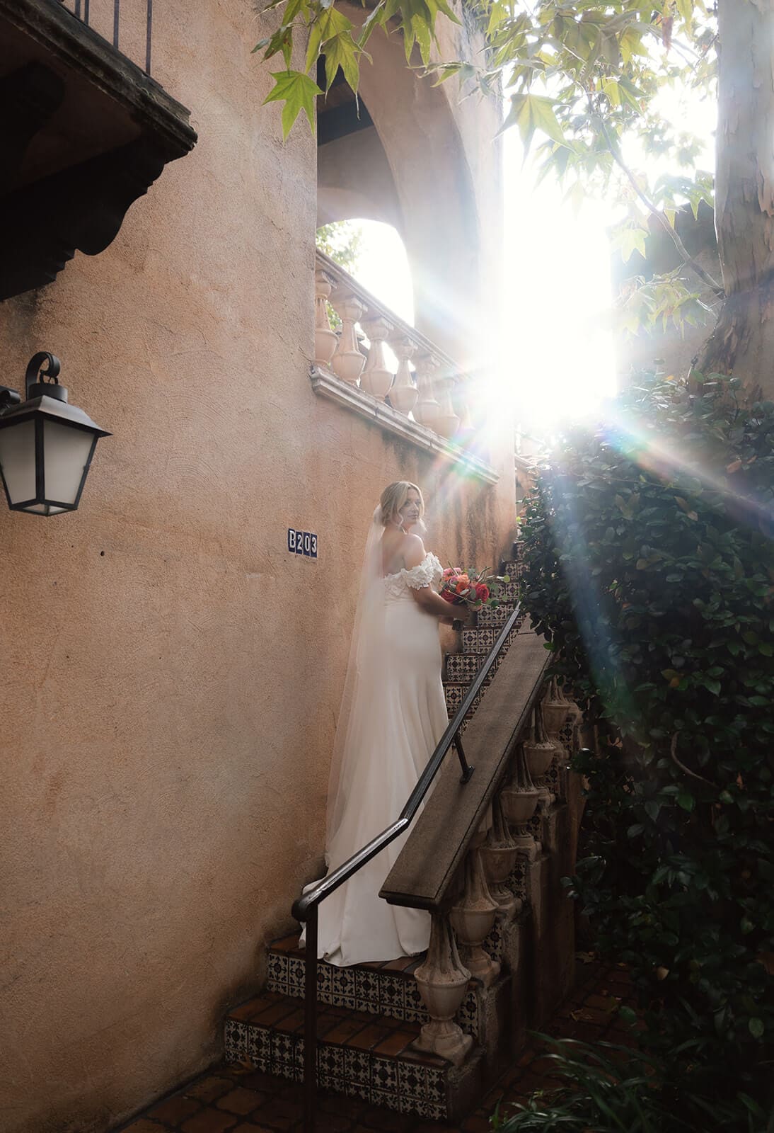 Bride standing on a staircase beside a stucco wall with sunlight streaming through the trees during a micro wedding at Tlaquepaque.
