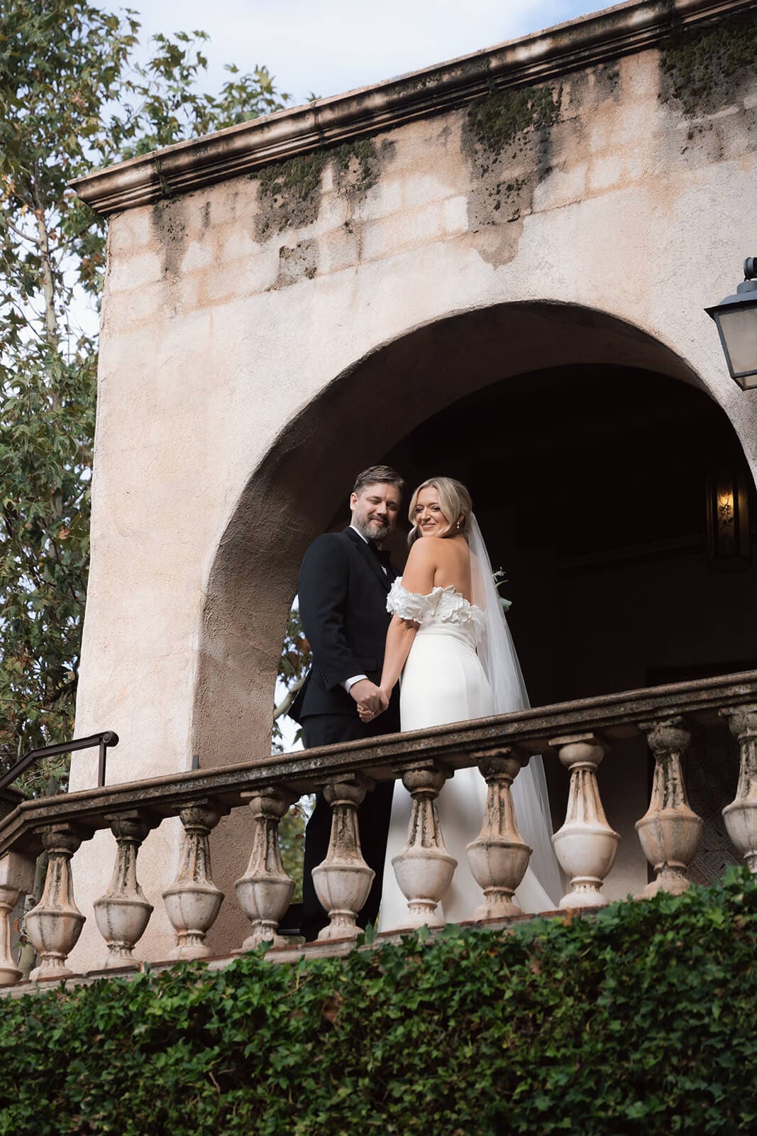 Bride and groom standing together beneath a large stucco archway with ivy-covered walls during a micro wedding at Tlaquepaque.