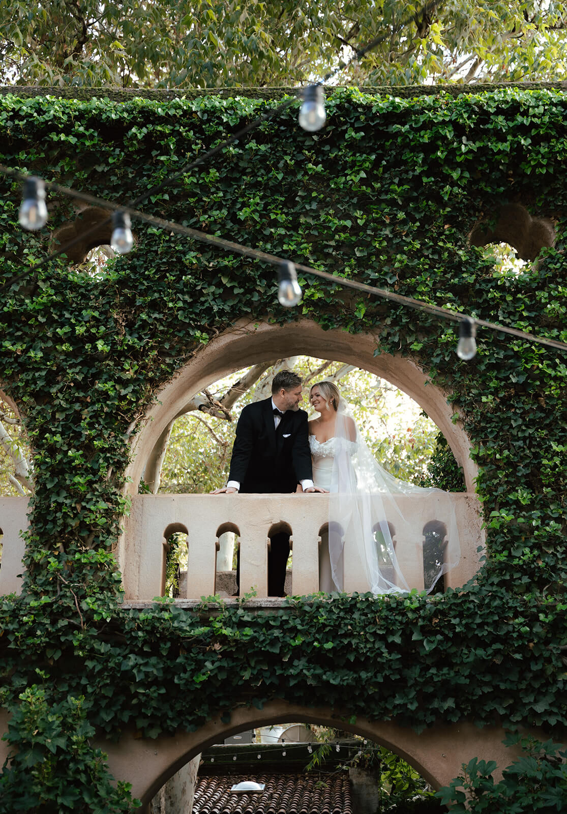 Newly married couple standing beneath an ivy-covered archway during an elegant garden elopement ceremony