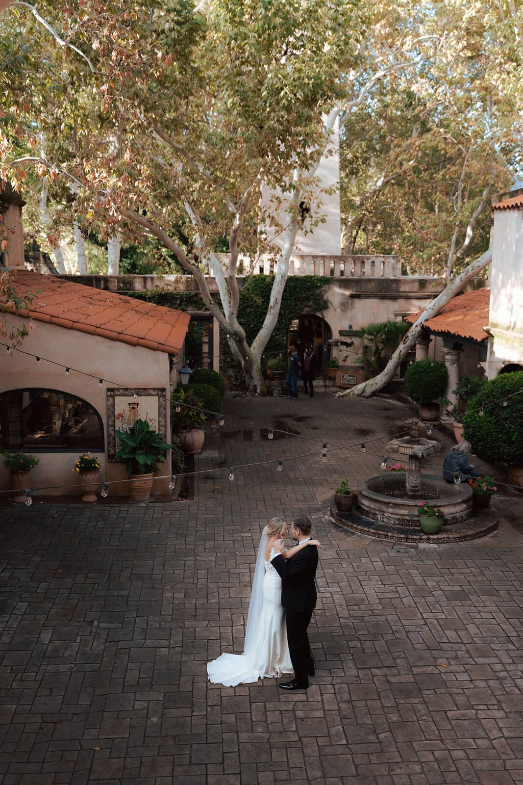 Bride and groom embracing in the center of a brick courtyard surrounded by Spanish-style architecture and trees during a micro wedding at Tlaquepaque.