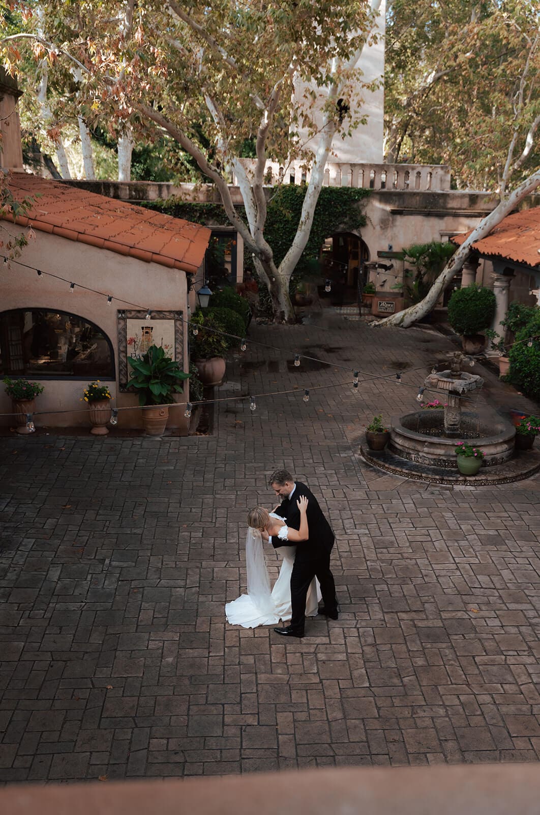 Bride and groom embracing in the center of a brick courtyard surrounded by Spanish-style architecture during a micro wedding at Tlaquepaque.
