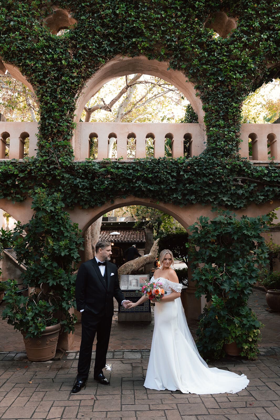 Bride and groom standing together beneath ivy-covered arches with Spanish-style architecture during a micro wedding at Tlaquepaque.