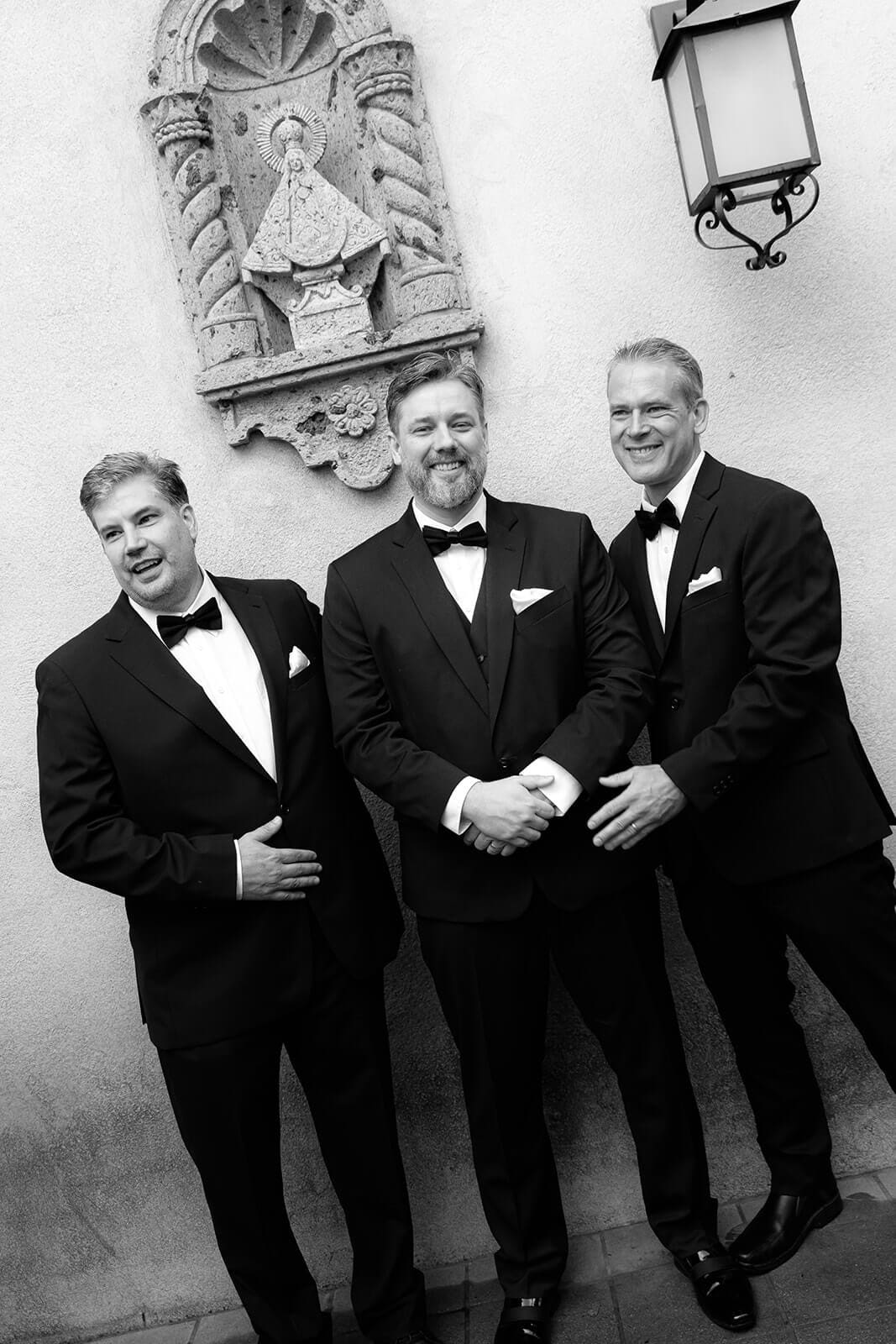 Black and white photo of three men in tuxedos standing together and smiling during a wedding at Tlaquepaque.