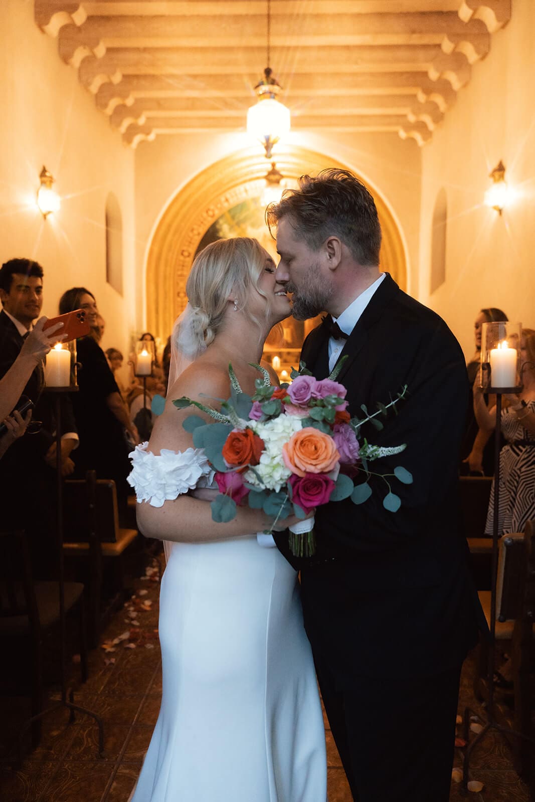 Bride and groom sharing their first kiss inside a candlelit chapel during an intimate elopement ceremony