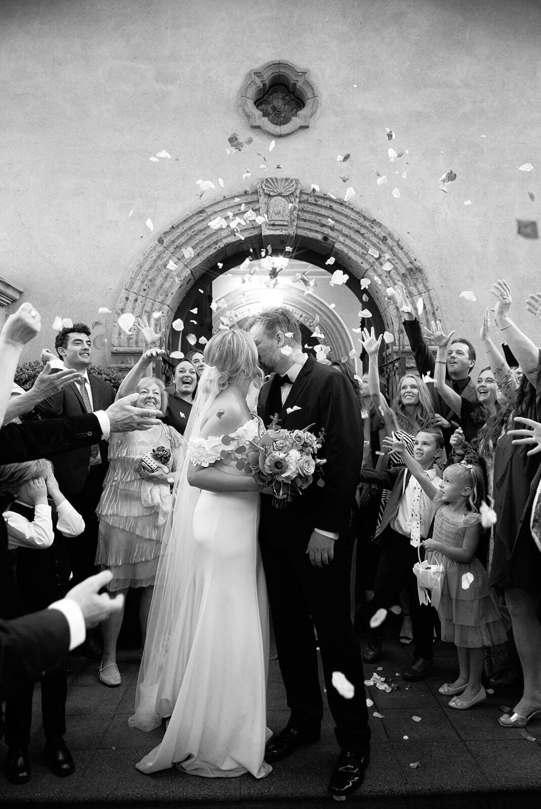 Black and white photo of newlyweds exiting a chapel while guests toss flower petals during a micro wedding at Tlaquepaque.