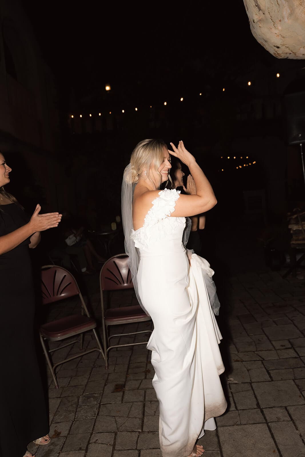 Bride dancing outdoors during an evening wedding reception with guests surrounding her.