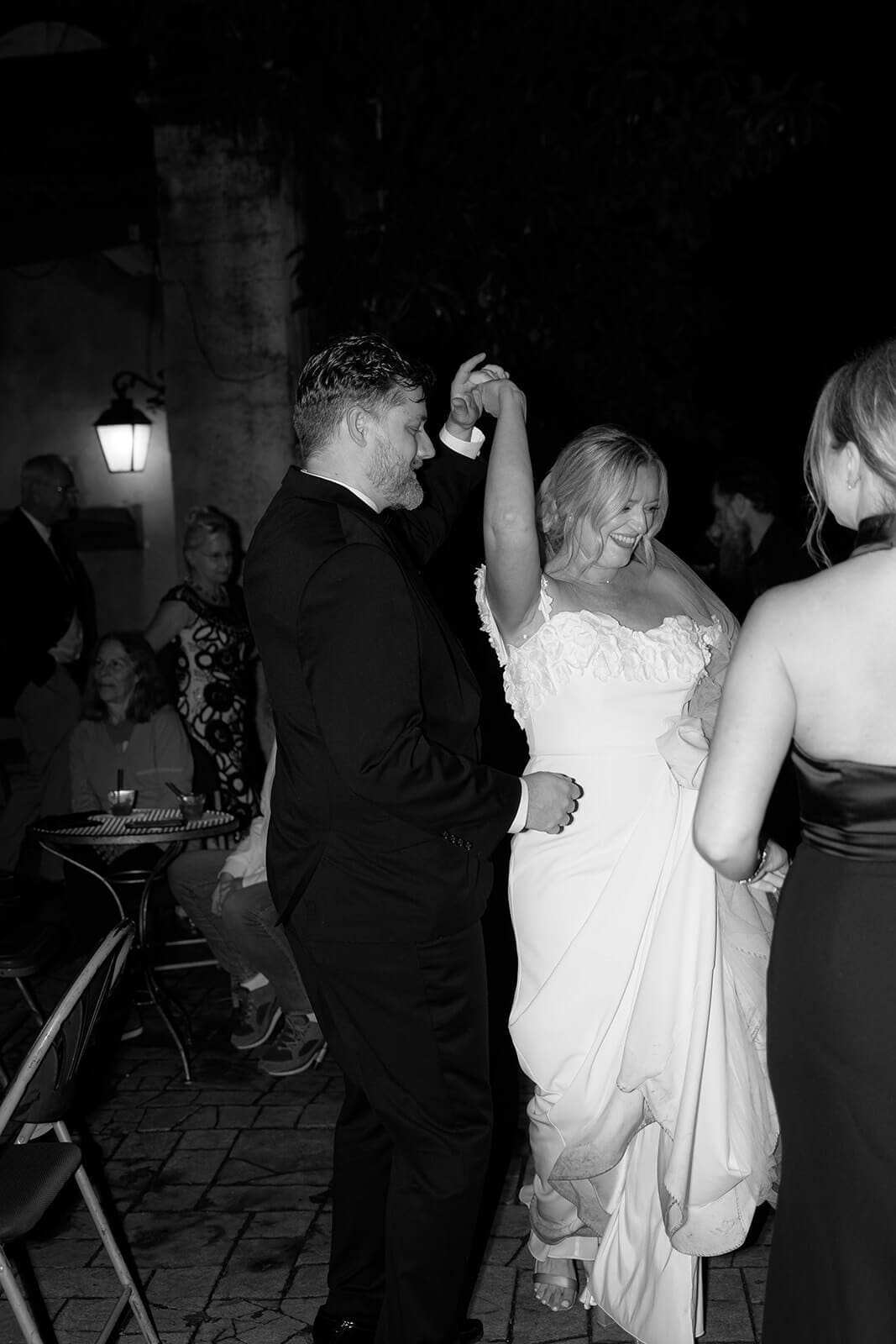 Black and white photo of guests dancing together during an outdoor wedding reception at night.