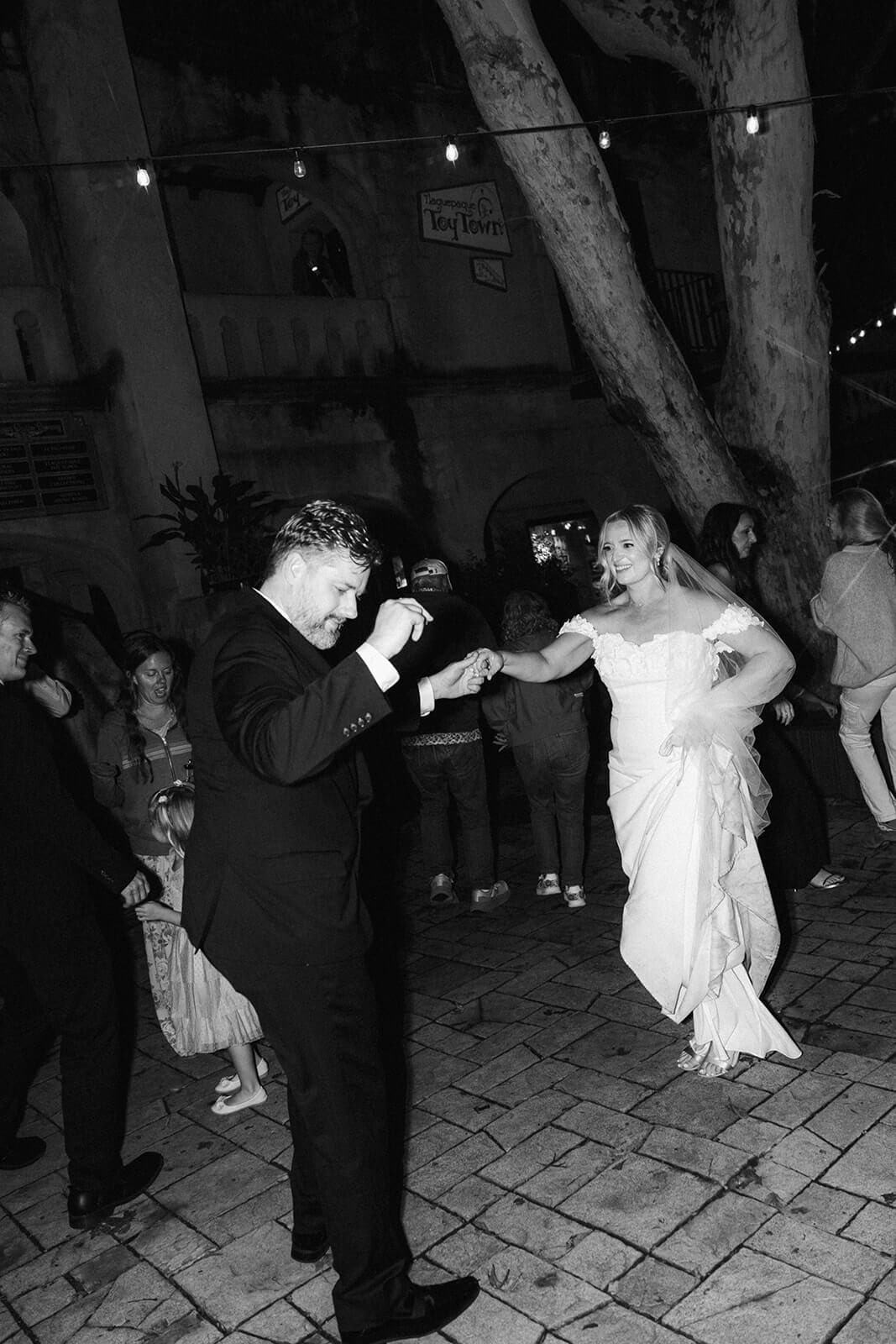 Black and white photo of guests dancing together outdoors during a wedding reception at night.