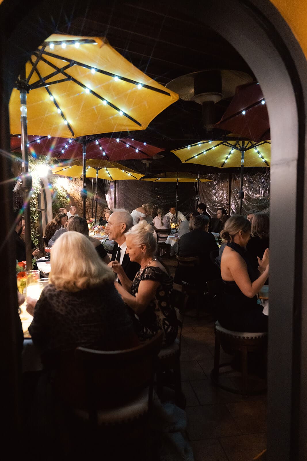 Outdoor wedding reception beneath glowing string lights and colorful umbrellas at night.