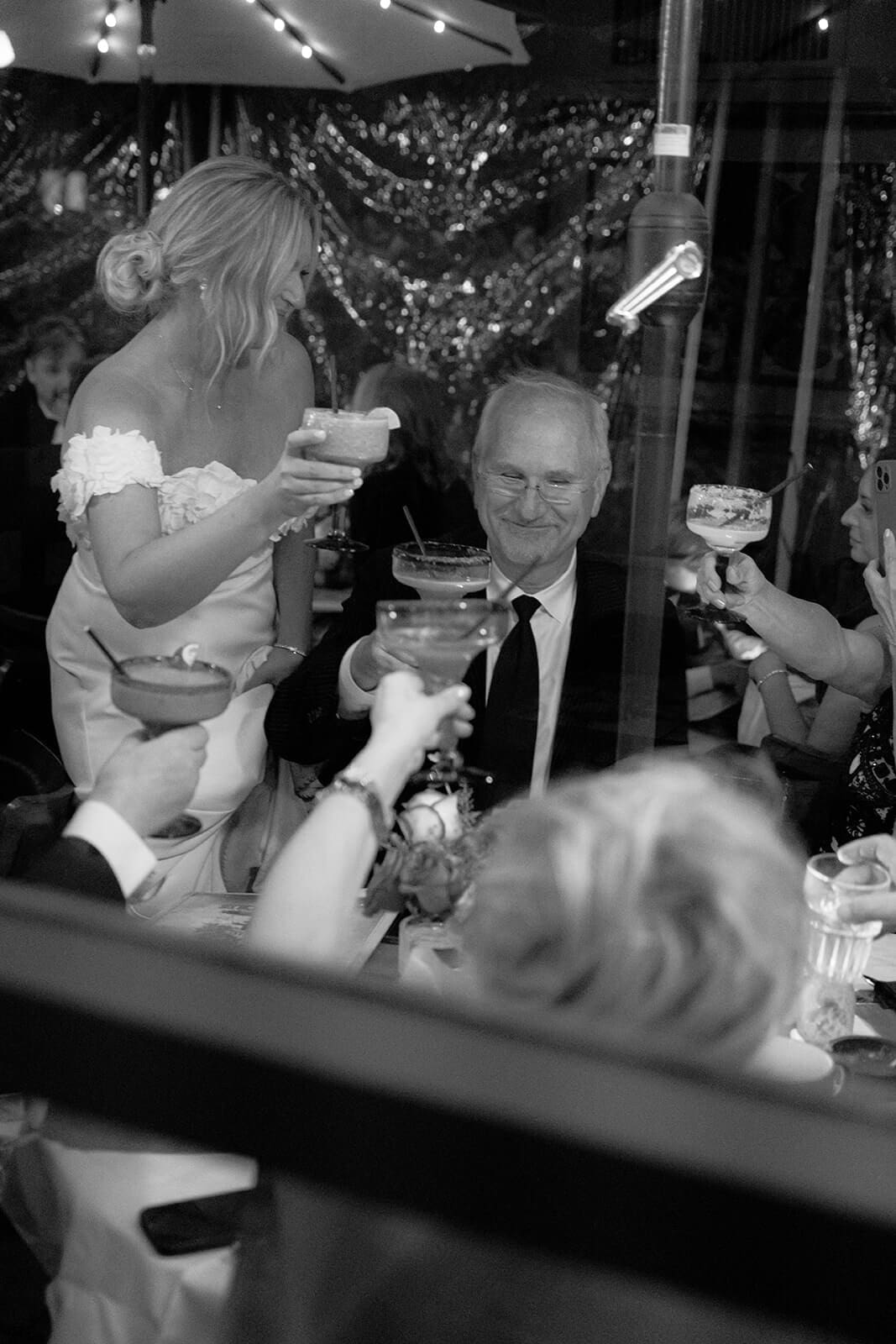 Black and white photo of guests raising drinks in celebration during an outdoor wedding reception.