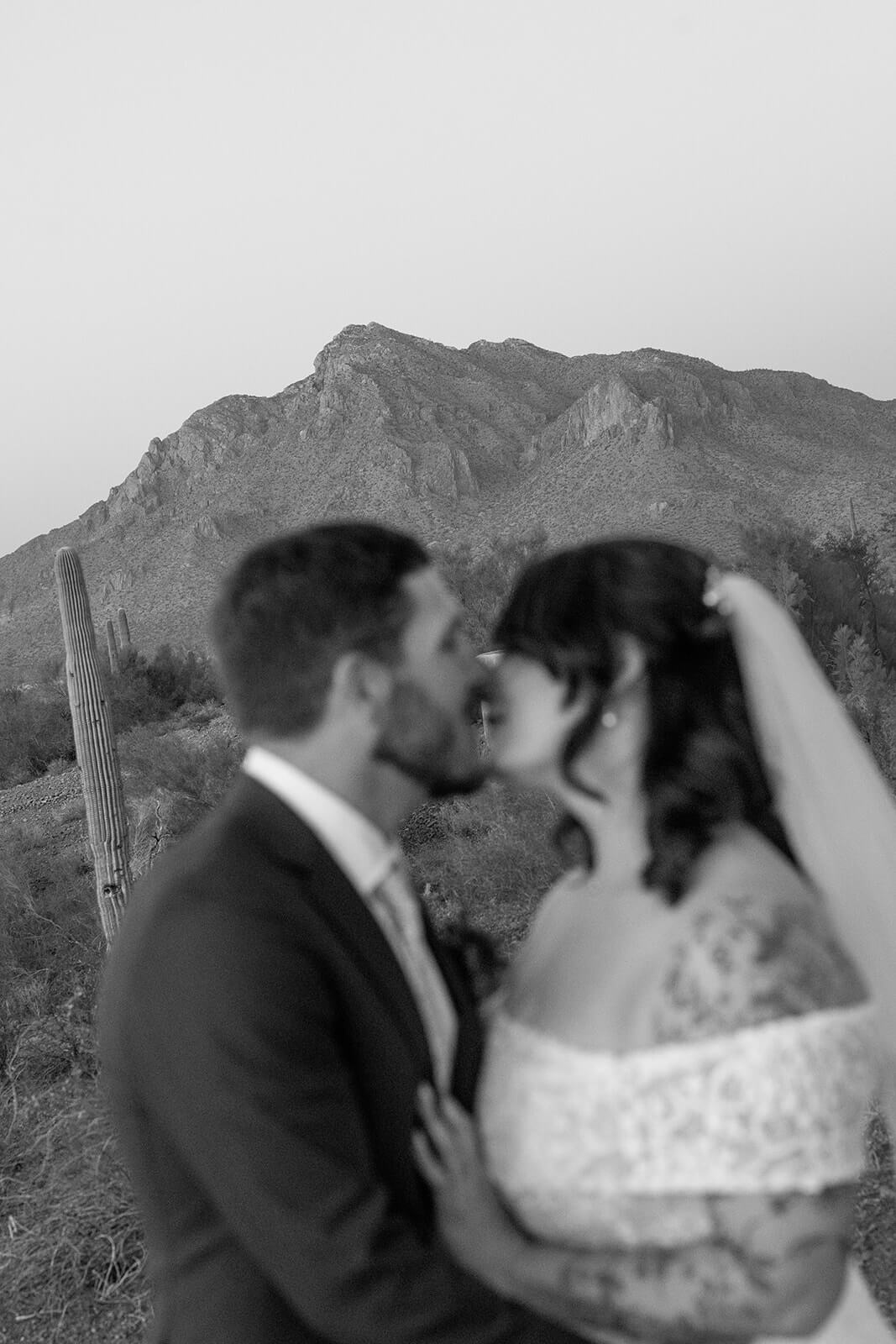 Black and white portrait of newly married couple kissing in the desert with mountain backdrop