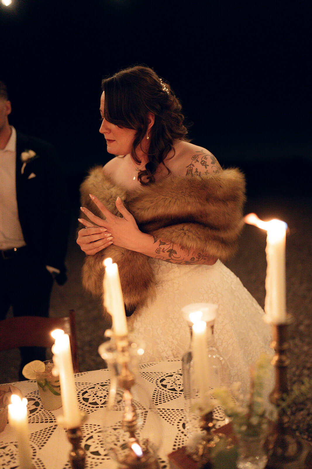Bride wrapped in a fur shawl during an intimate nighttime elopement reception lit by candles
