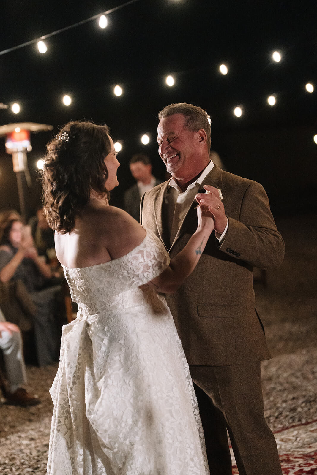 Bride dancing with her father during an emotional outdoor micro wedding reception beneath glowing string lights