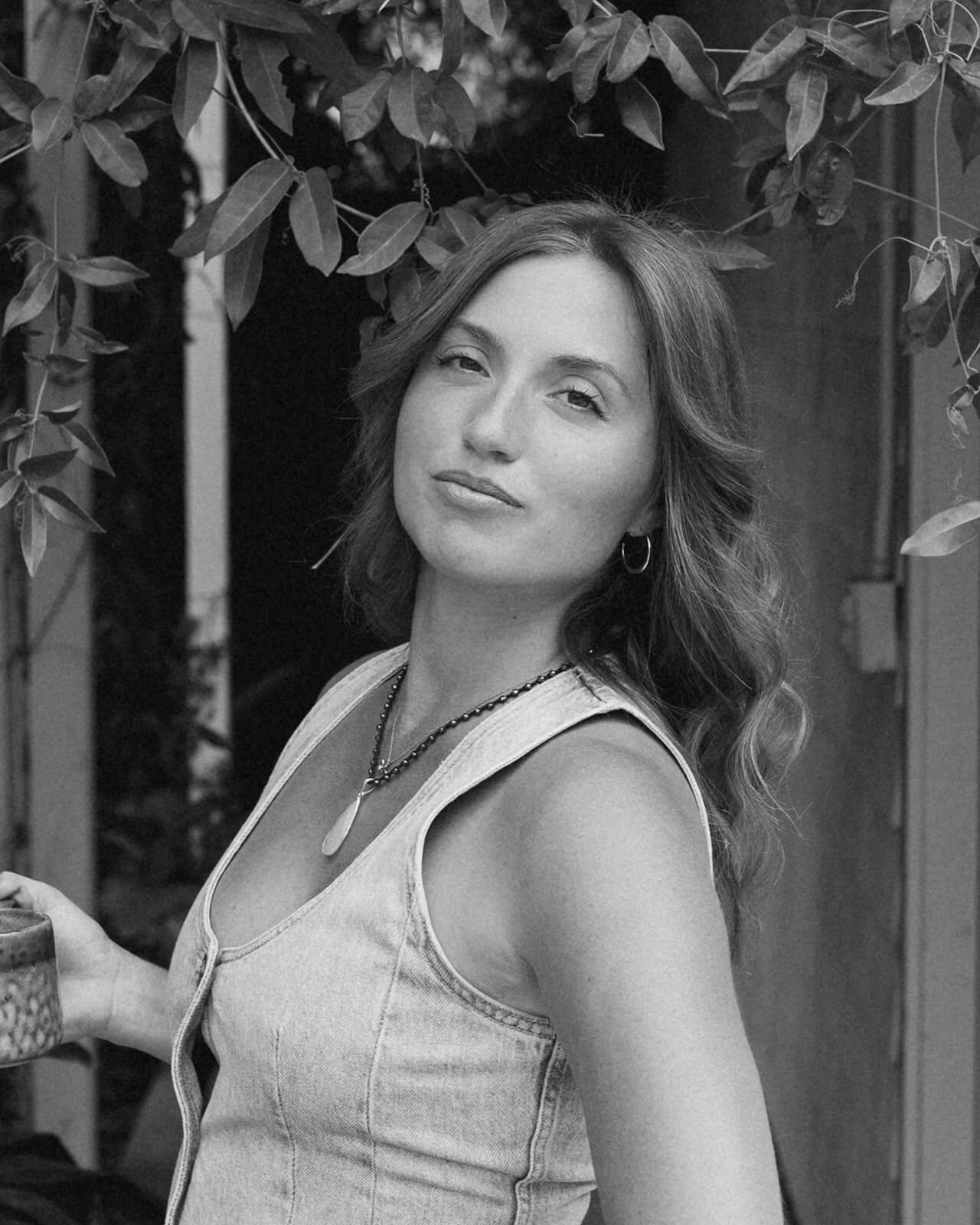 A black and white portrait of a woman looking back over her shoulder beneath an archway of tropical leaves at The Bloomstead in Arizona.