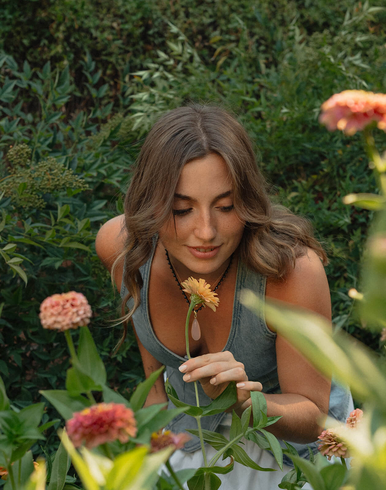 A woman looks down softly while surrounded by blooming orange and pink zinnias in the flower fields at The Bloomstead flower farm in Arizona.