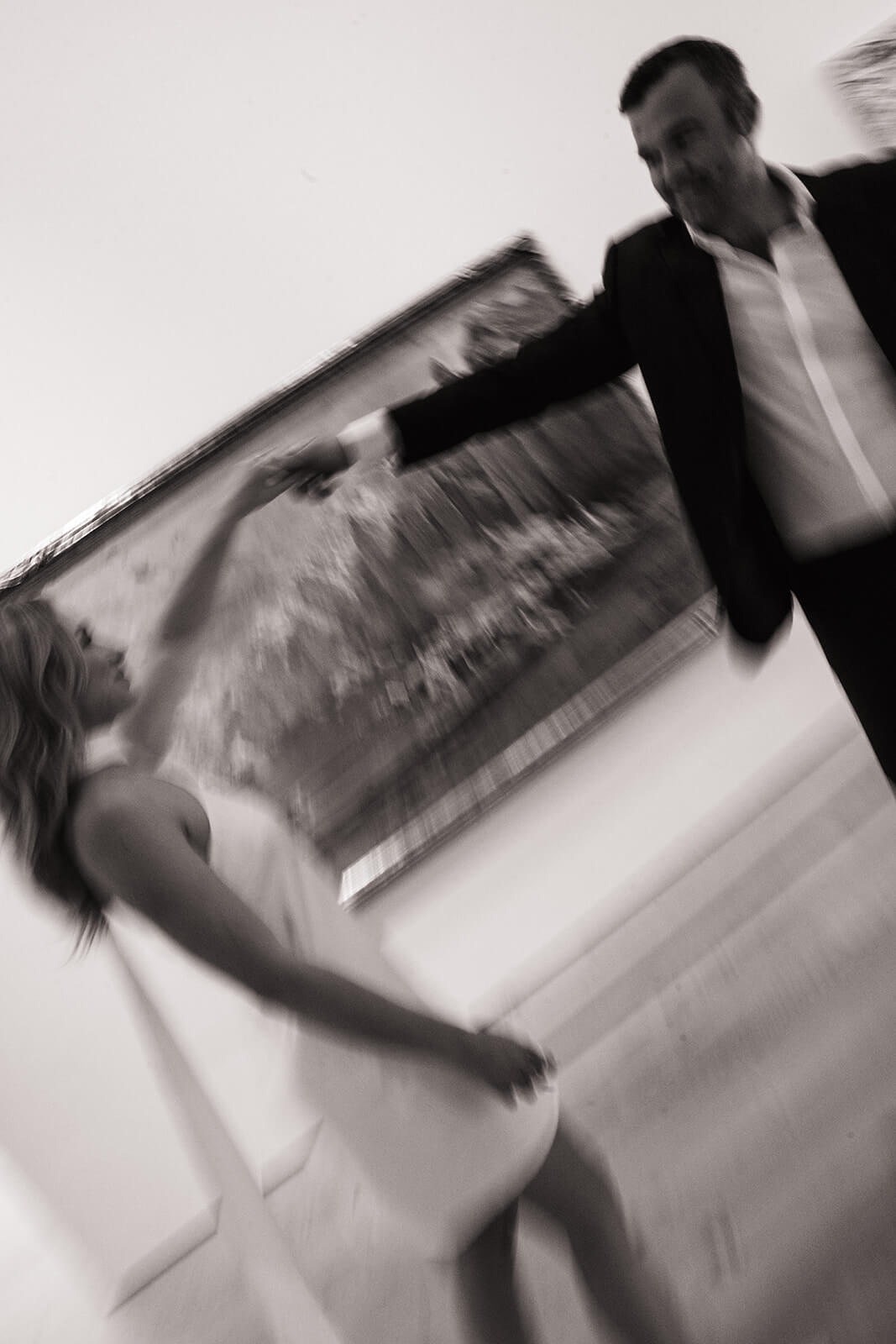 A motion-blurred black and white photo of a couple spinning and dancing together inside the Phoenix Art Museum, a framed painting and white gallery walls sweeping behind them.