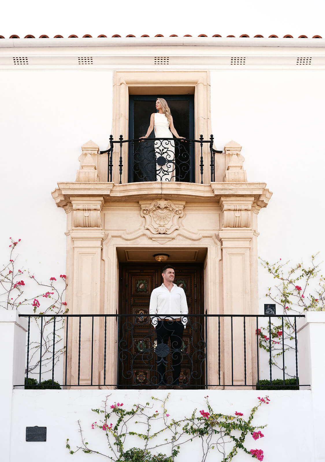 A couple poses on separate balconies of the ornate Spanish-style facade at Wrigley Mansion, one of the most cinematic engagement photoshoot locations in Phoenix, the woman on the upper balcony and her partner standing below in the doorway.