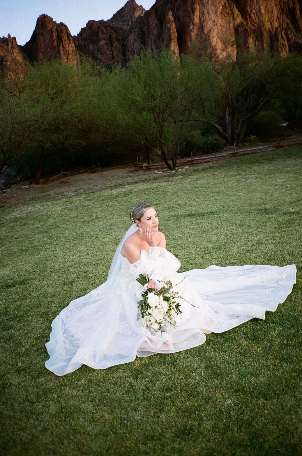 Bride sitting in the grass holding her bouquet with her veil and dress spread around her at Saguaro Lake Guest Ranch wedding venue in Mesa Arizona
