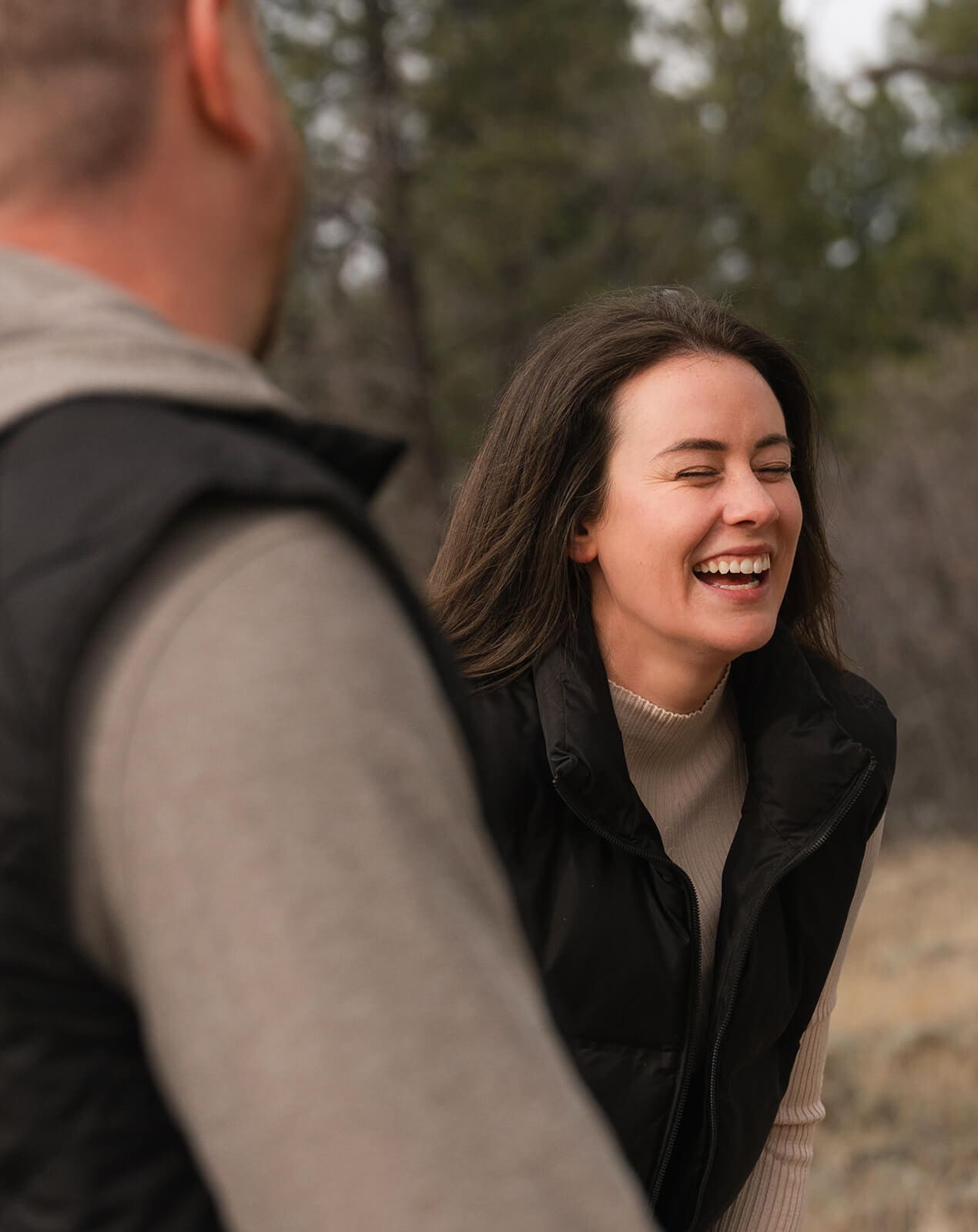Close-up of a woman laughing with joy during a proposal, shot over her partner's shoulder, her expression full of happy surprise.
