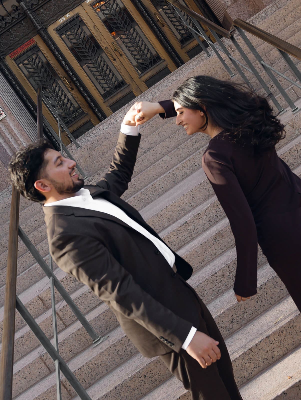 A playful shot of a couple on decorative building steps, the man leaning back dramatically while the woman laughs above him.
