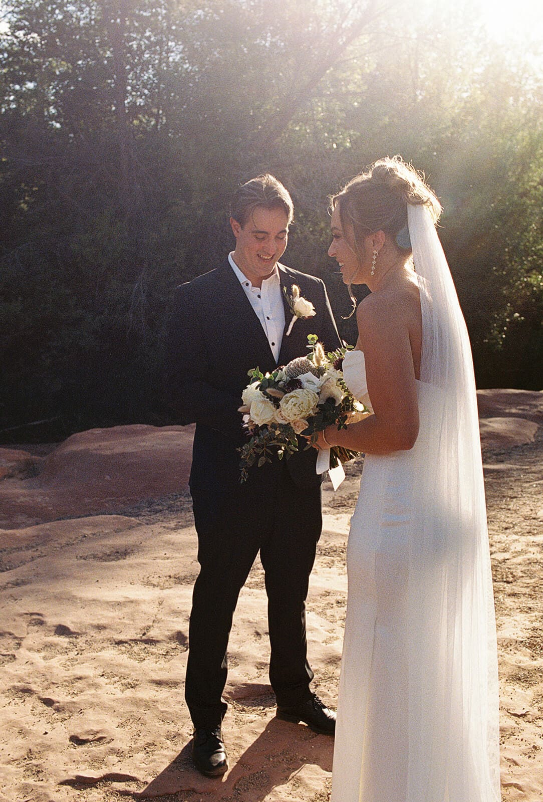 Bride and groom standing together in warm golden light during their Sedona elopement portraits beside the creek and surrounding greenery.