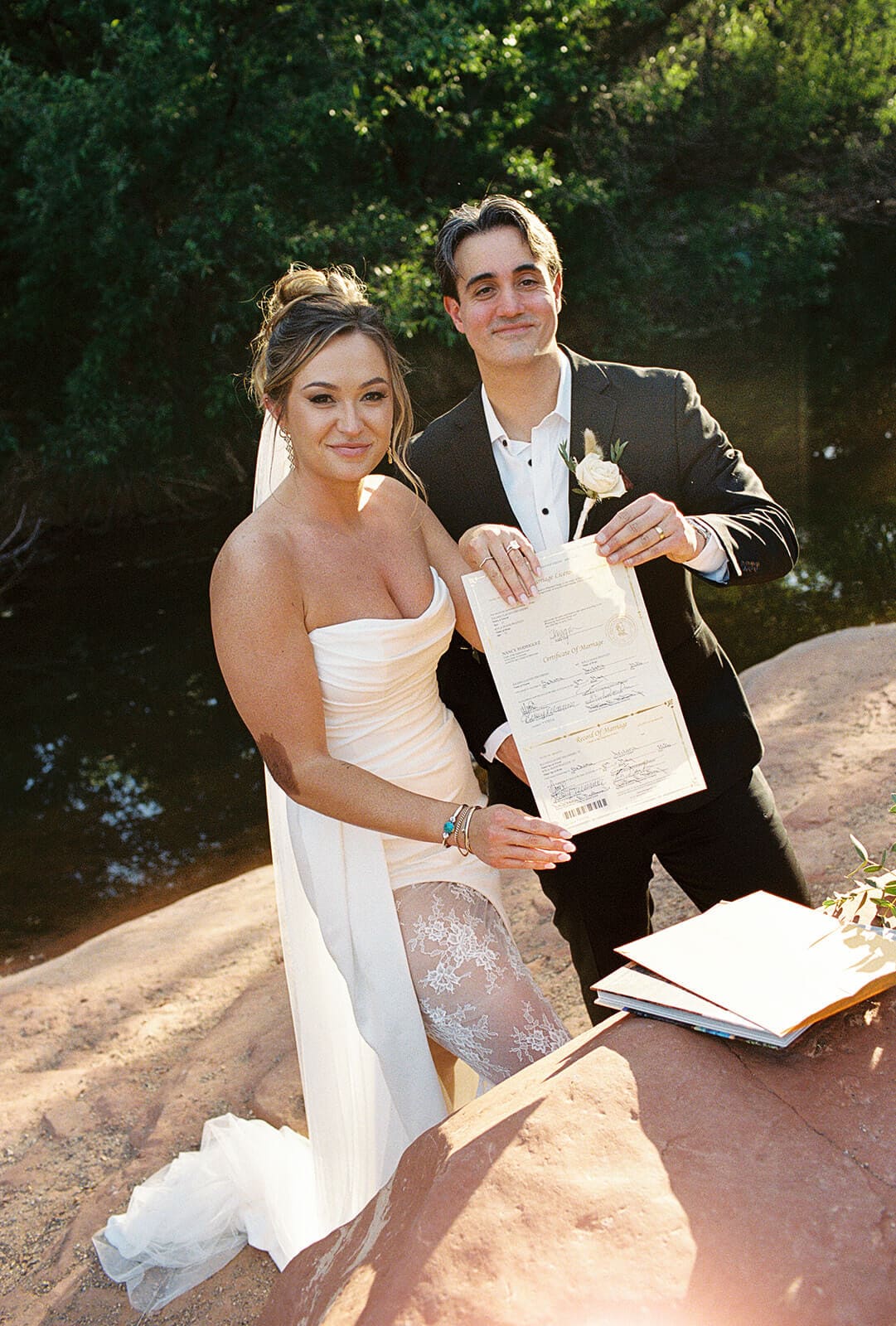 Bride and groom signing their marriage license after their Sedona elopement ceremony beside the creek, with vow books and flowers nearby.
