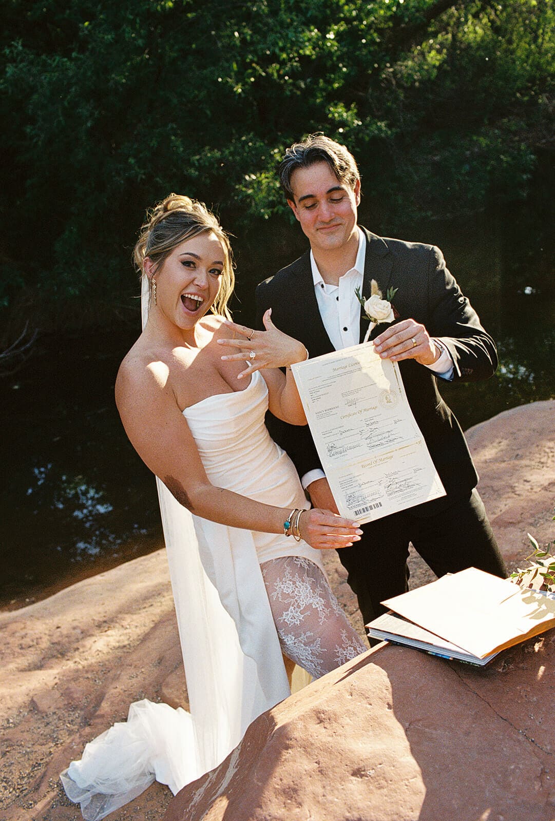 Newlyweds showing off their marriage license and wedding rings after their elopement ceremony beside the water.