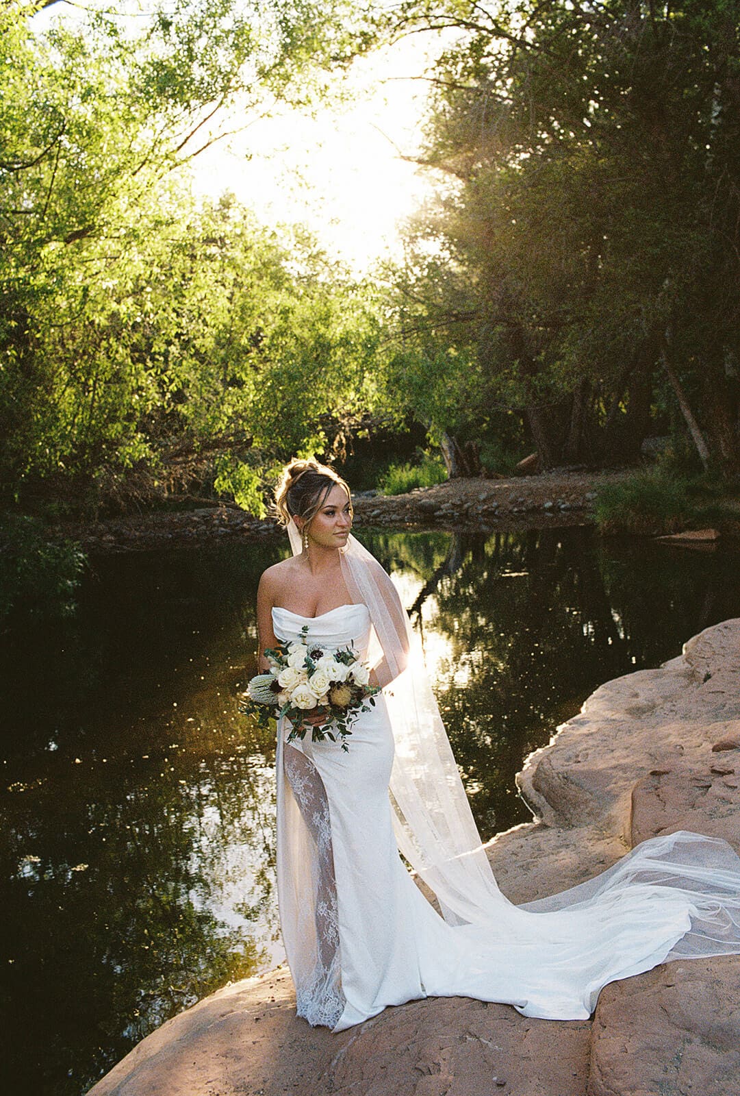 Bride holding her bouquet in bright golden backlight during a Sedona elopement portrait near the creek and lush greenery.