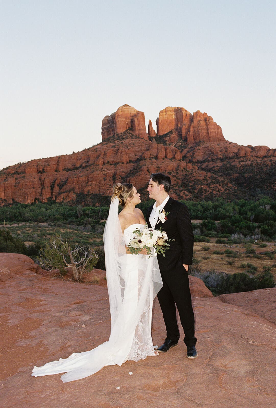 Bride and groom standing together on the red rocks during their Sedona elopement portraits, with Cathedral Rock rising in the distance.