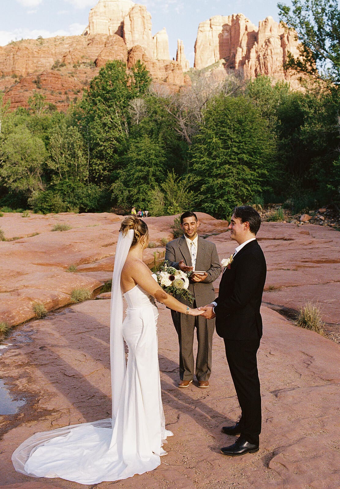 Couple exchanging rings during their Sedona elopement ceremony, surrounded by red rocks, desert trees, and soft evening light.