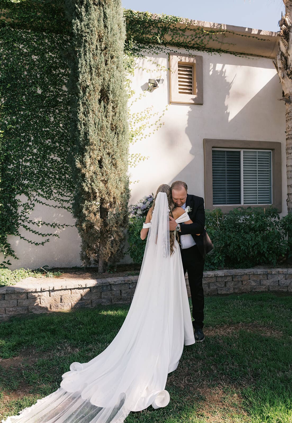 Bride embracing her father in an emotional moment on the tree-lined grounds at Knotty Barn wedding venue in Queen Creek Arizona
